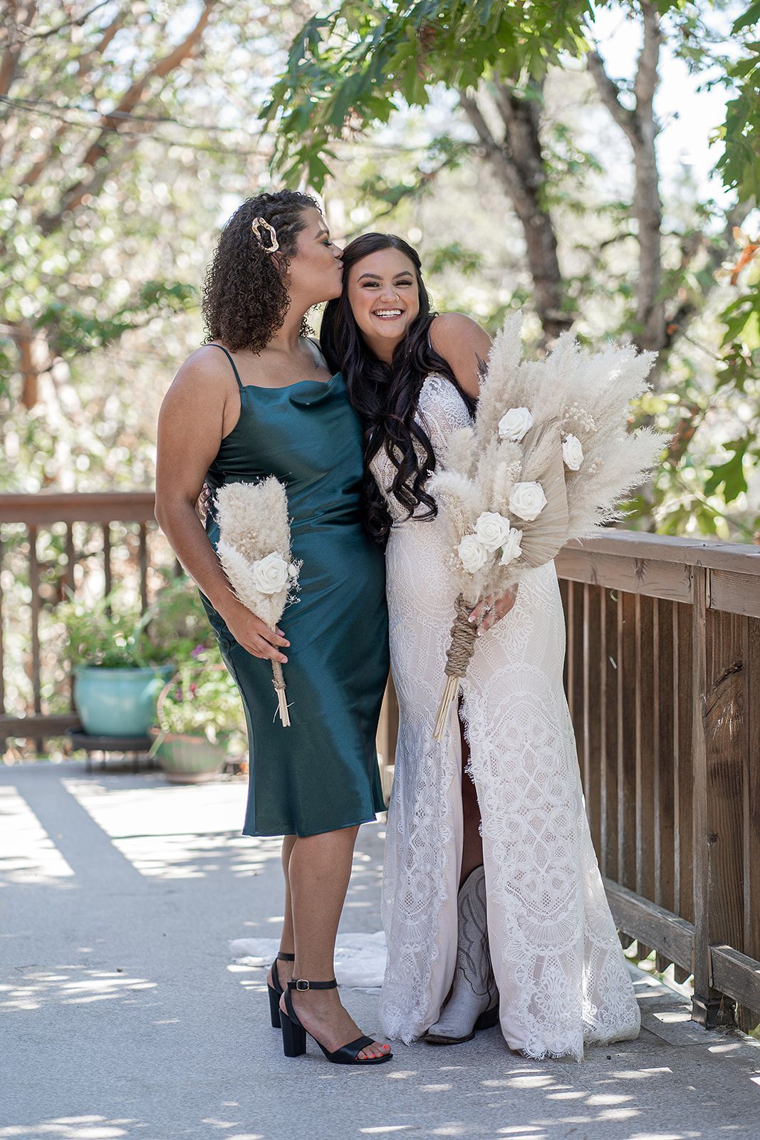 A bride and her bridesmaid are posing for a picture and the bride is kissing her bridesmaid on the cheek.