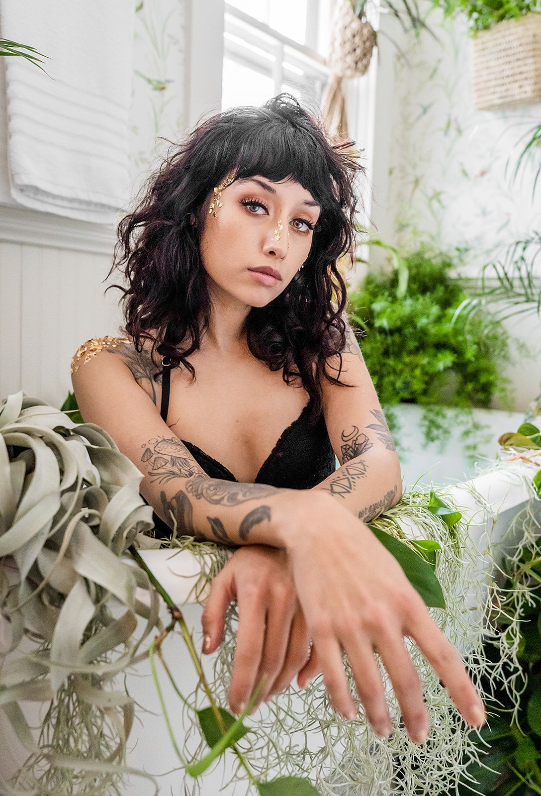 A woman is sitting in a bathtub surrounded by plants.