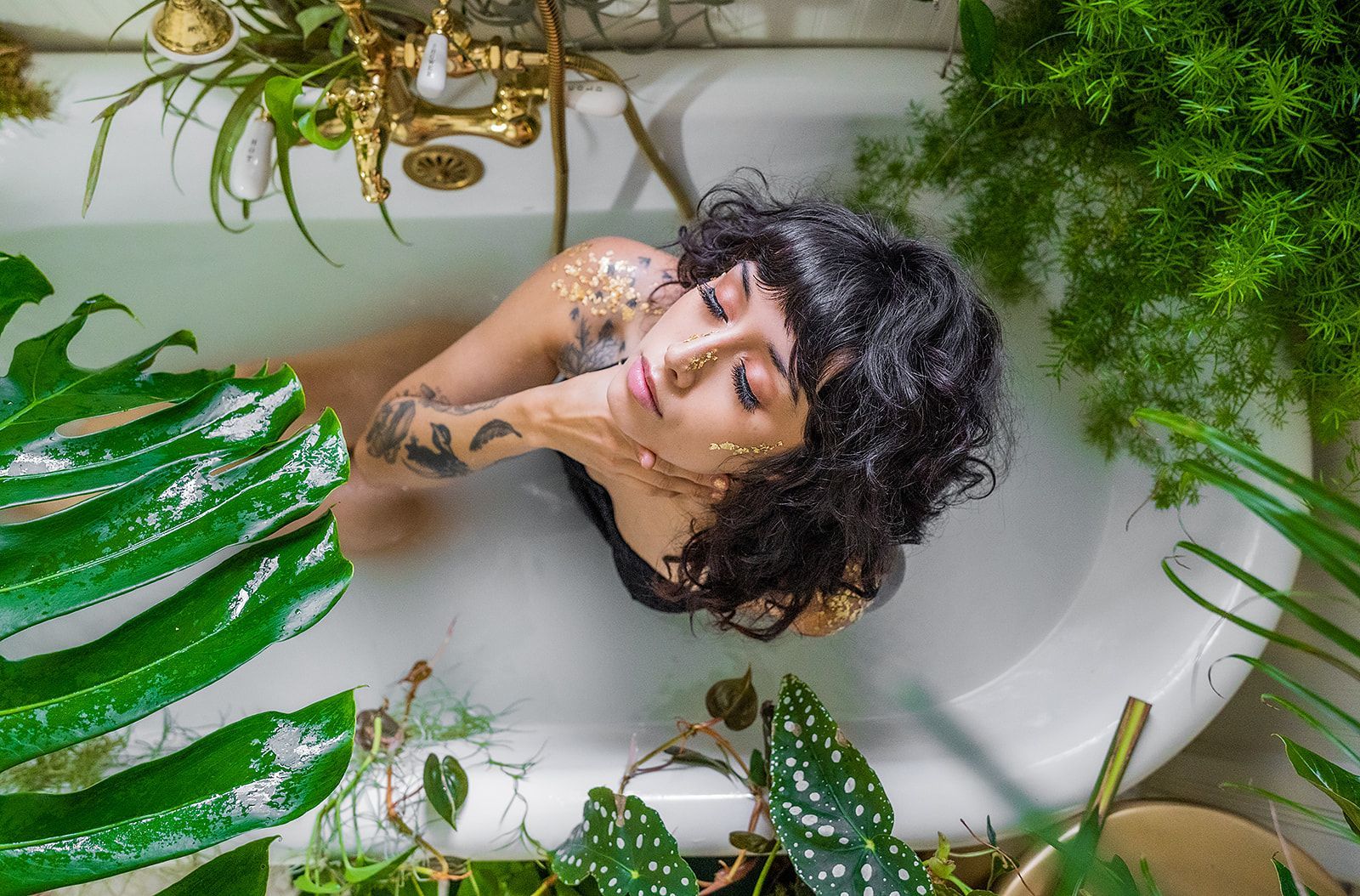 A woman is laying in a bathtub filled with milk, surrounded by plants.