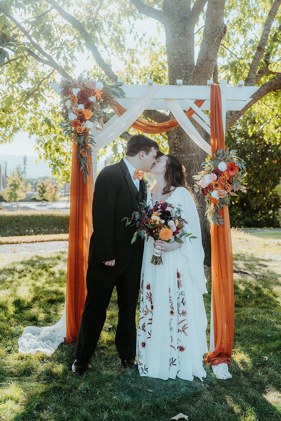 A bride and groom are kissing under an arch at their wedding.
