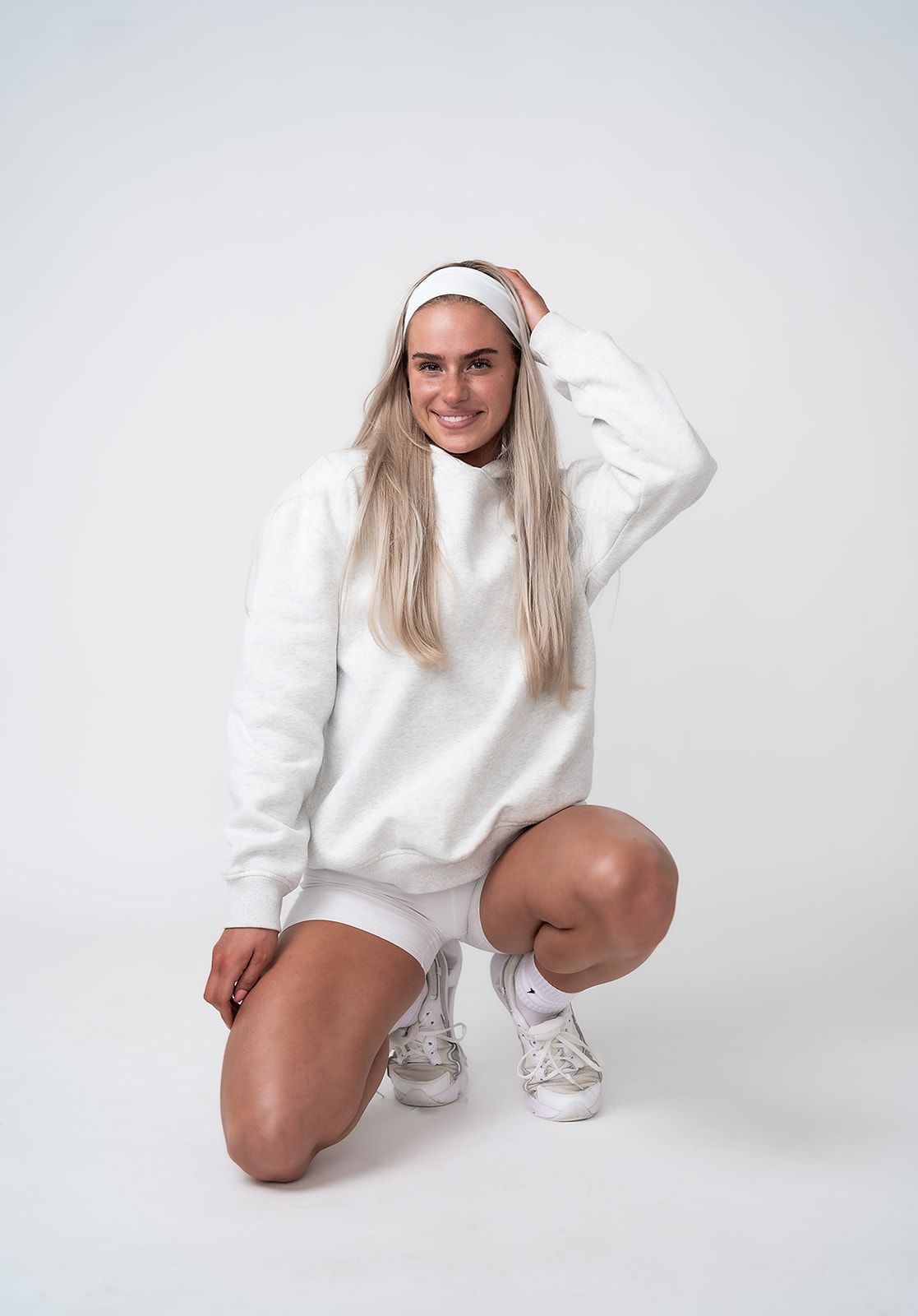 A woman in a white sweatshirt and shorts is squatting down on a white background.