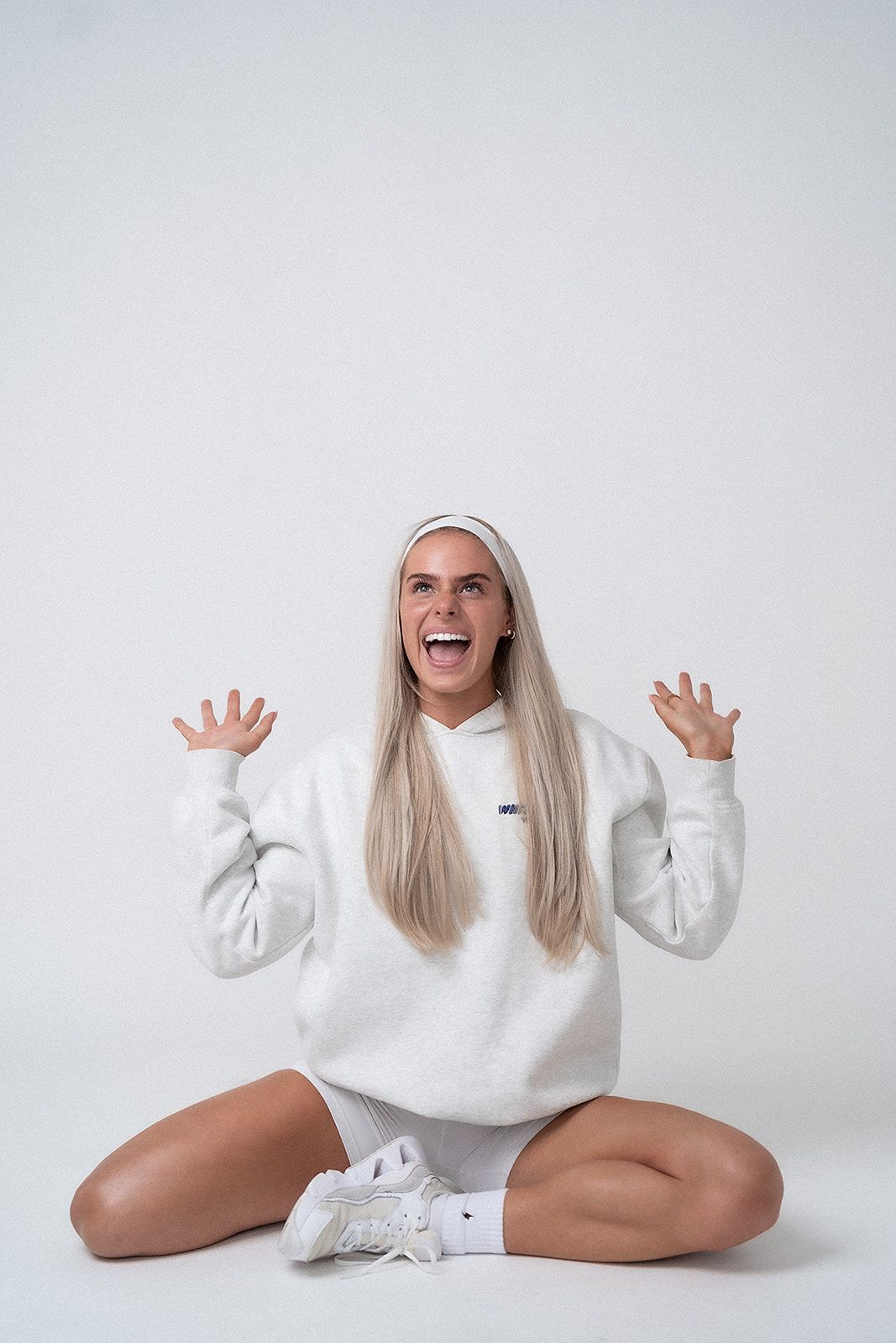 A woman in a white hoodie is sitting on the floor with her legs crossed.