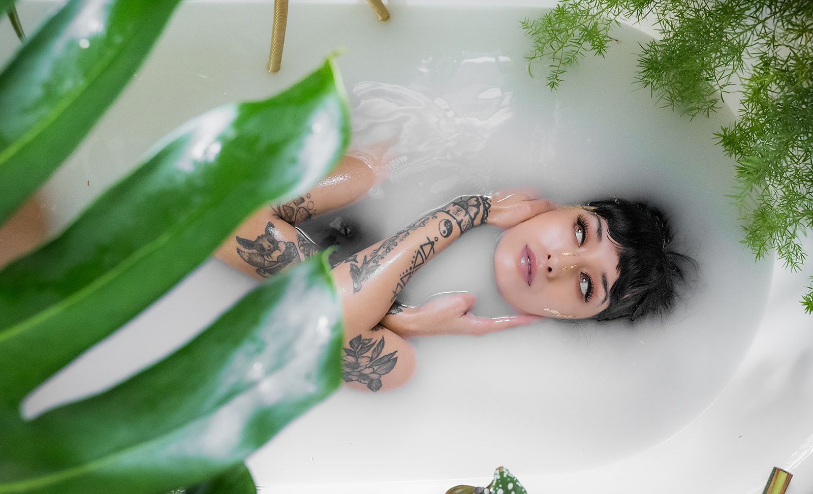 A woman is laying in a bathtub filled with milk and leaves.