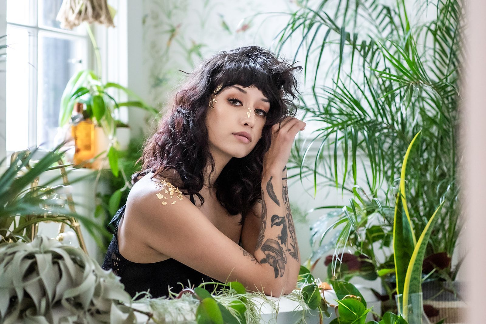 A woman is sitting in a room surrounded by plants.