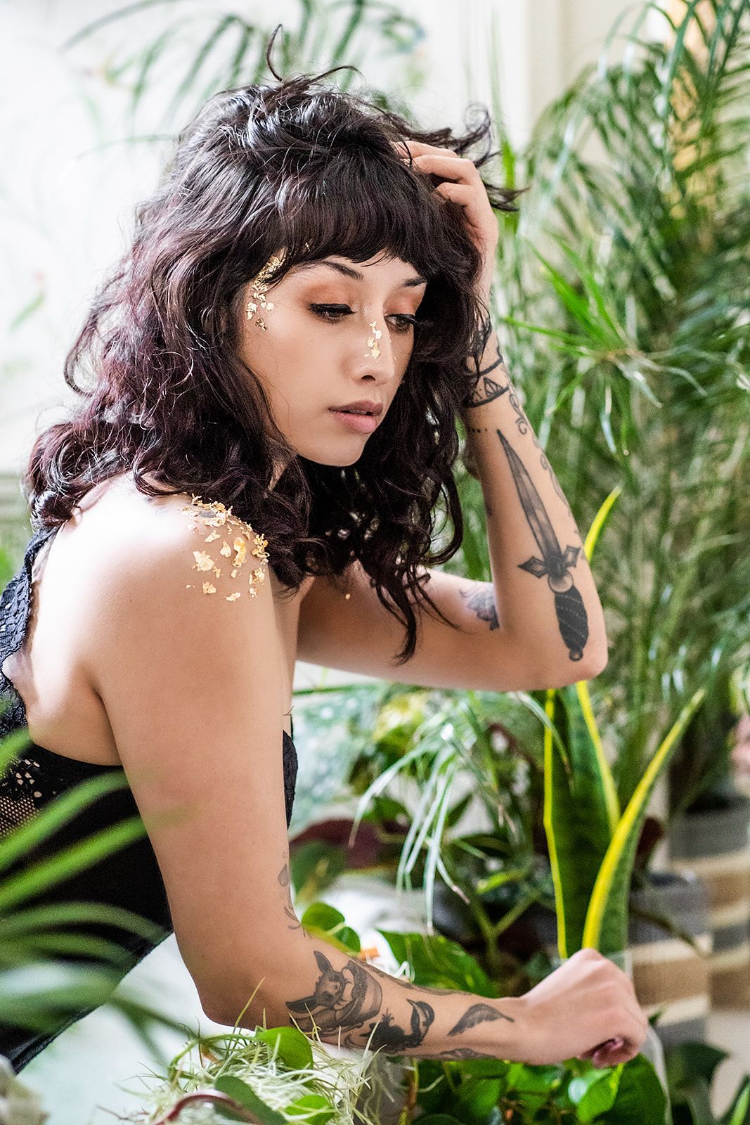 A woman with tattoos is standing in front of a bunch of plants.