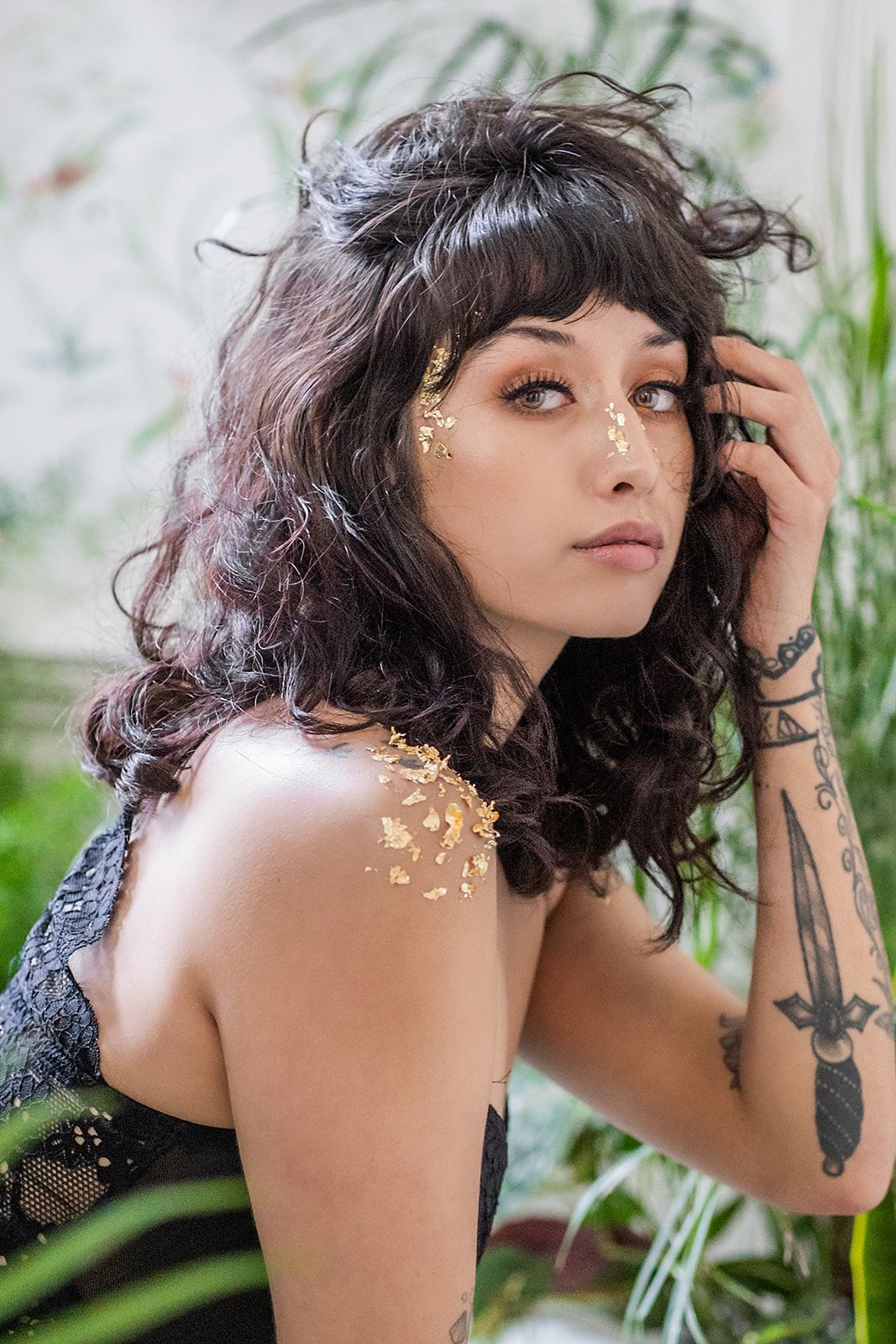A woman with a tattoo on her arm is standing in front of a plant.