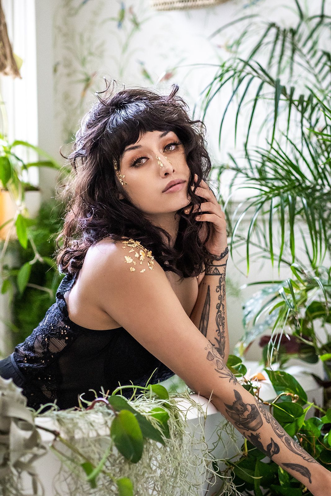 A woman in a black dress is sitting in a bathtub surrounded by plants.