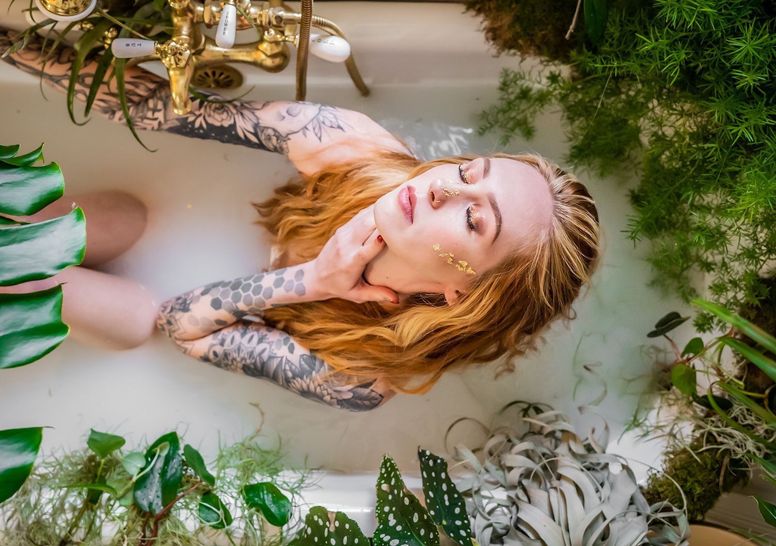 A woman is laying in a bathtub surrounded by plants.