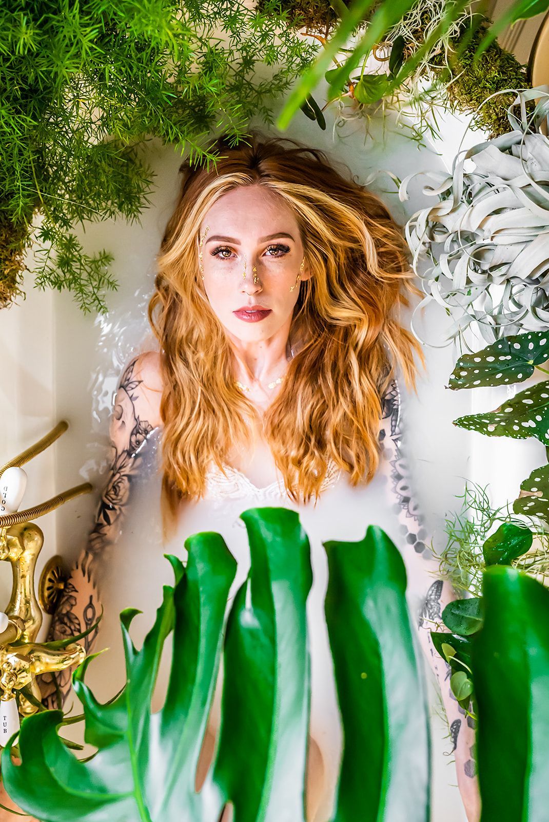 A woman is laying in a bathtub surrounded by plants.