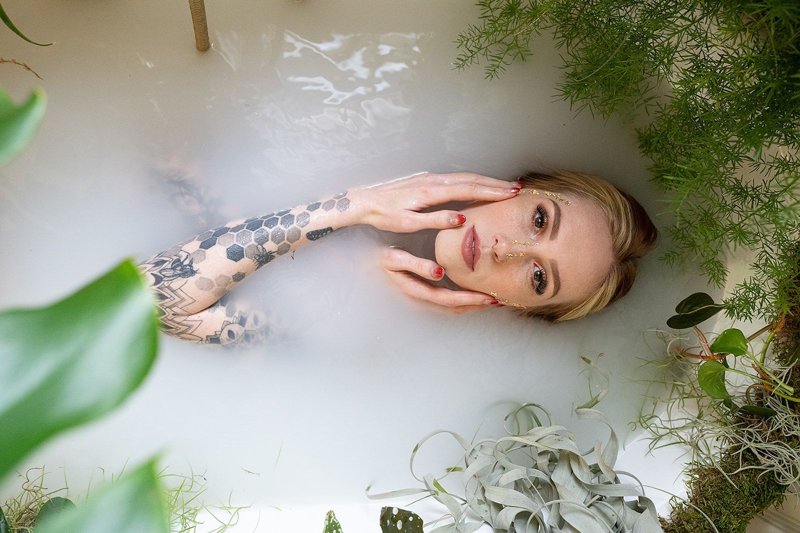 A woman is laying in a bathtub filled with milk and plants.
