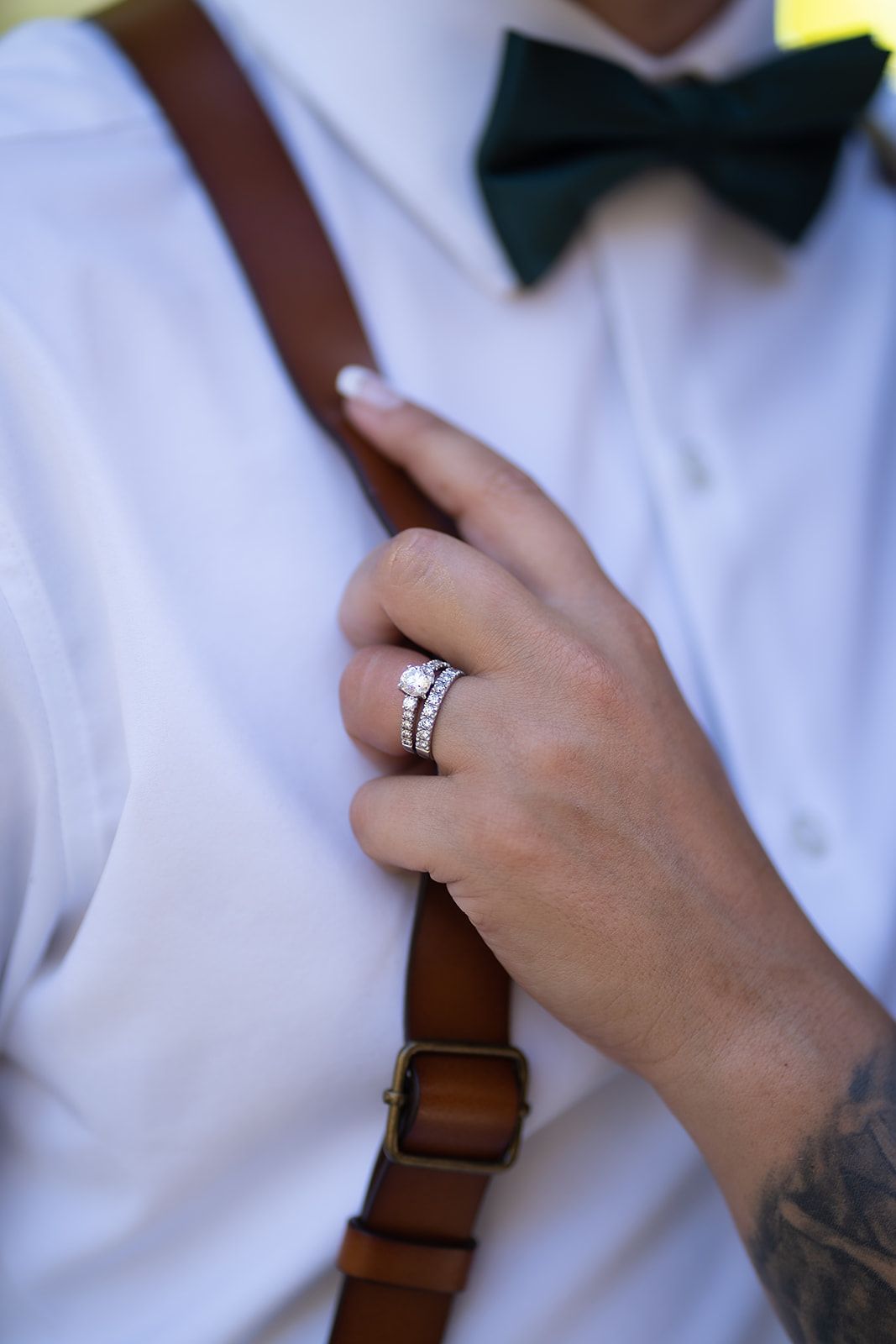 A man wearing suspenders and a bow tie has a wedding ring on his finger.