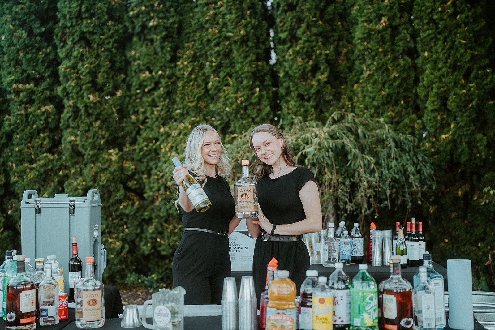 Two women are standing in front of a bar holding bottles of alcohol.