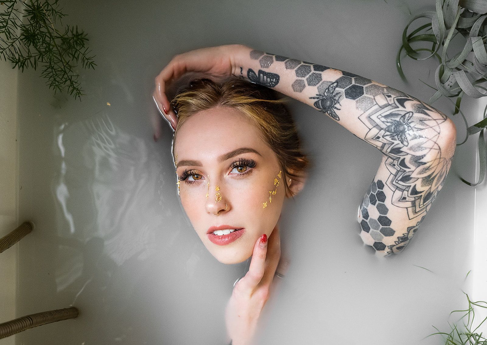 A woman with tattoos is laying in a bathtub filled with milk.
