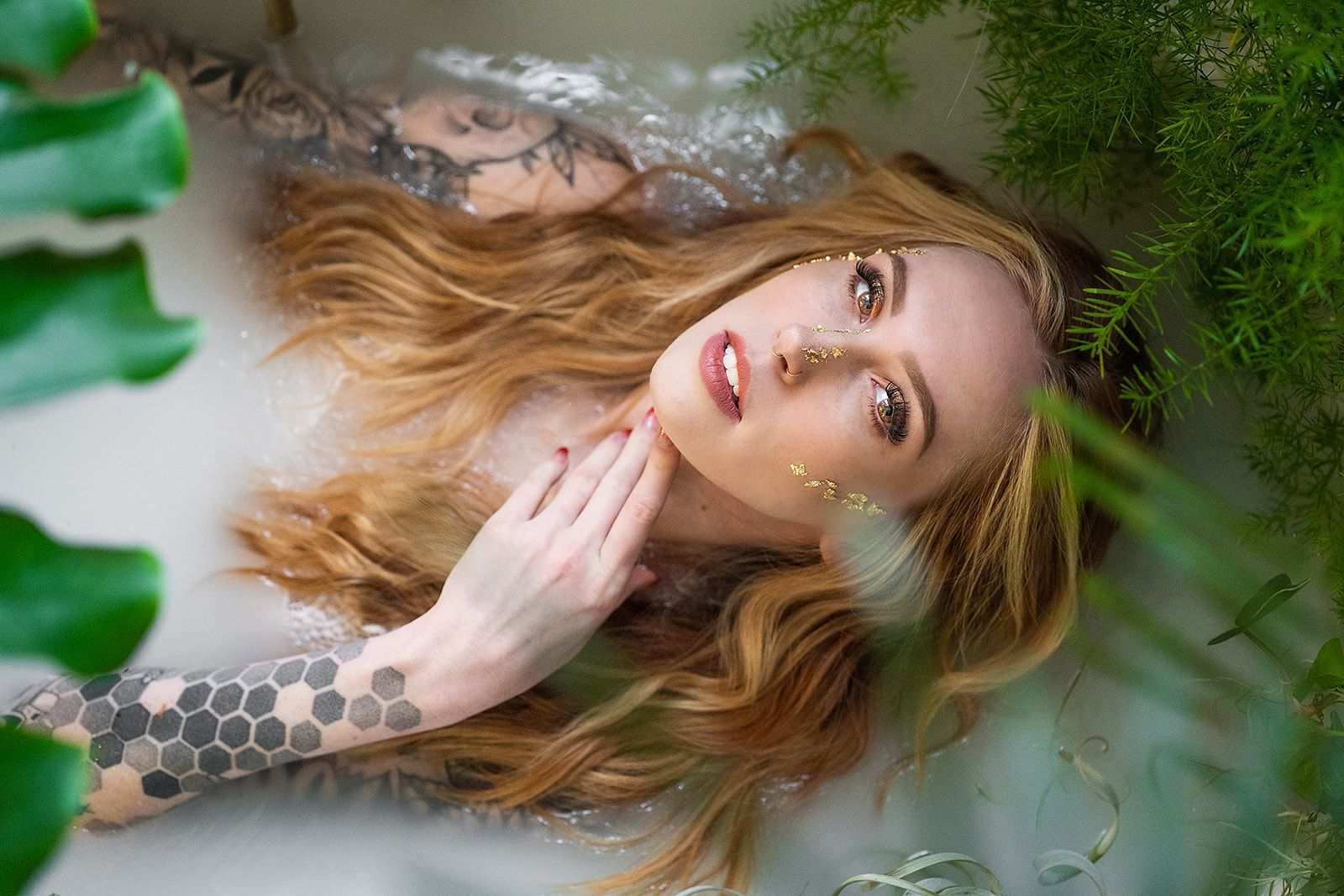 A woman is laying in a bathtub surrounded by plants.