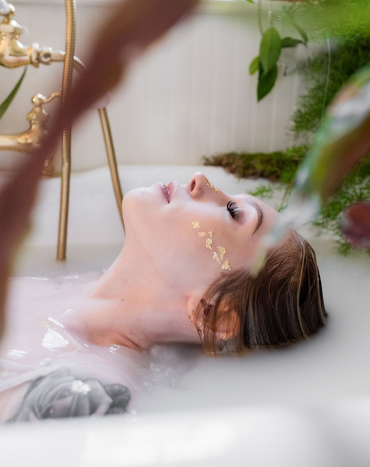 A woman is laying in a bathtub with a plant in the background.