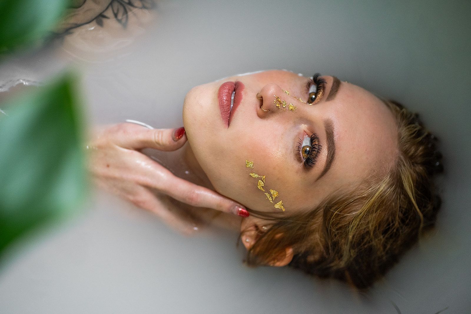 A woman is laying in a bathtub with a gold leaf on her face.