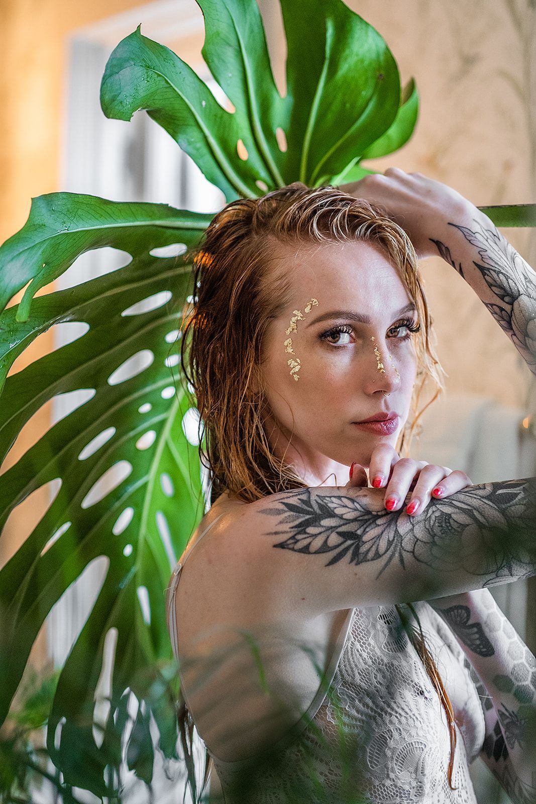 A woman with tattoos is standing in front of a plant.