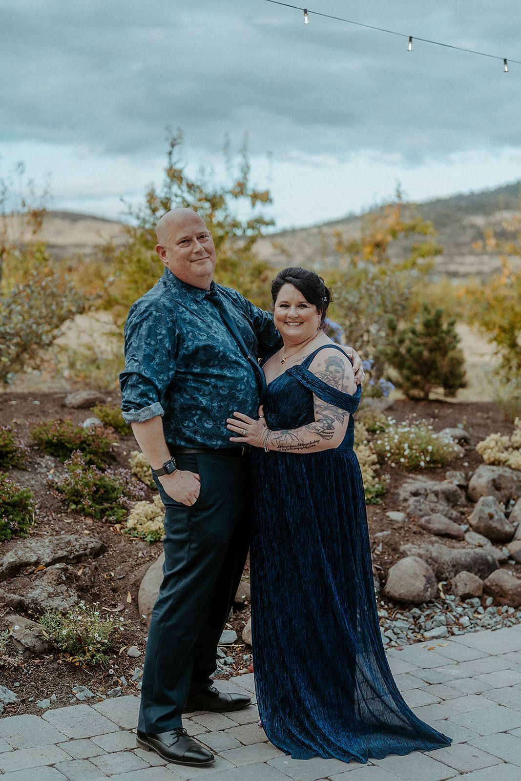 A man and a woman are posing for a picture together . the woman is wearing a blue dress.