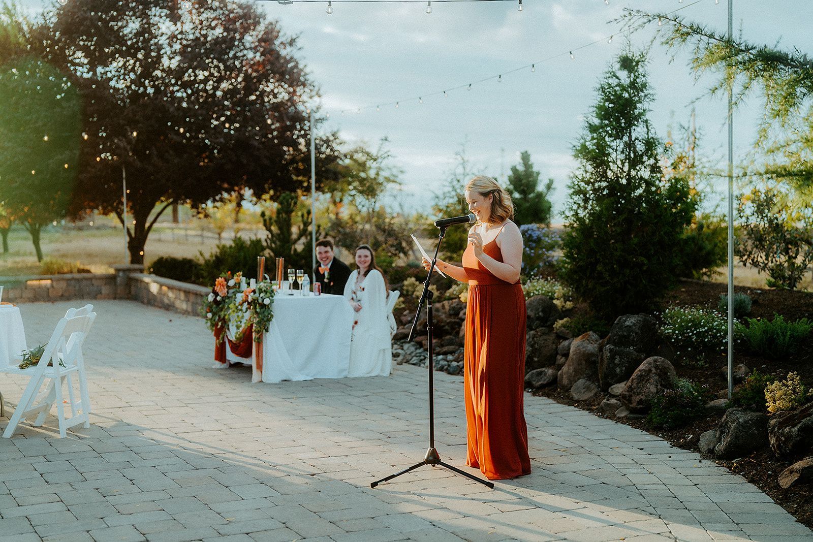 A woman in a red dress is giving a speech at a wedding reception.