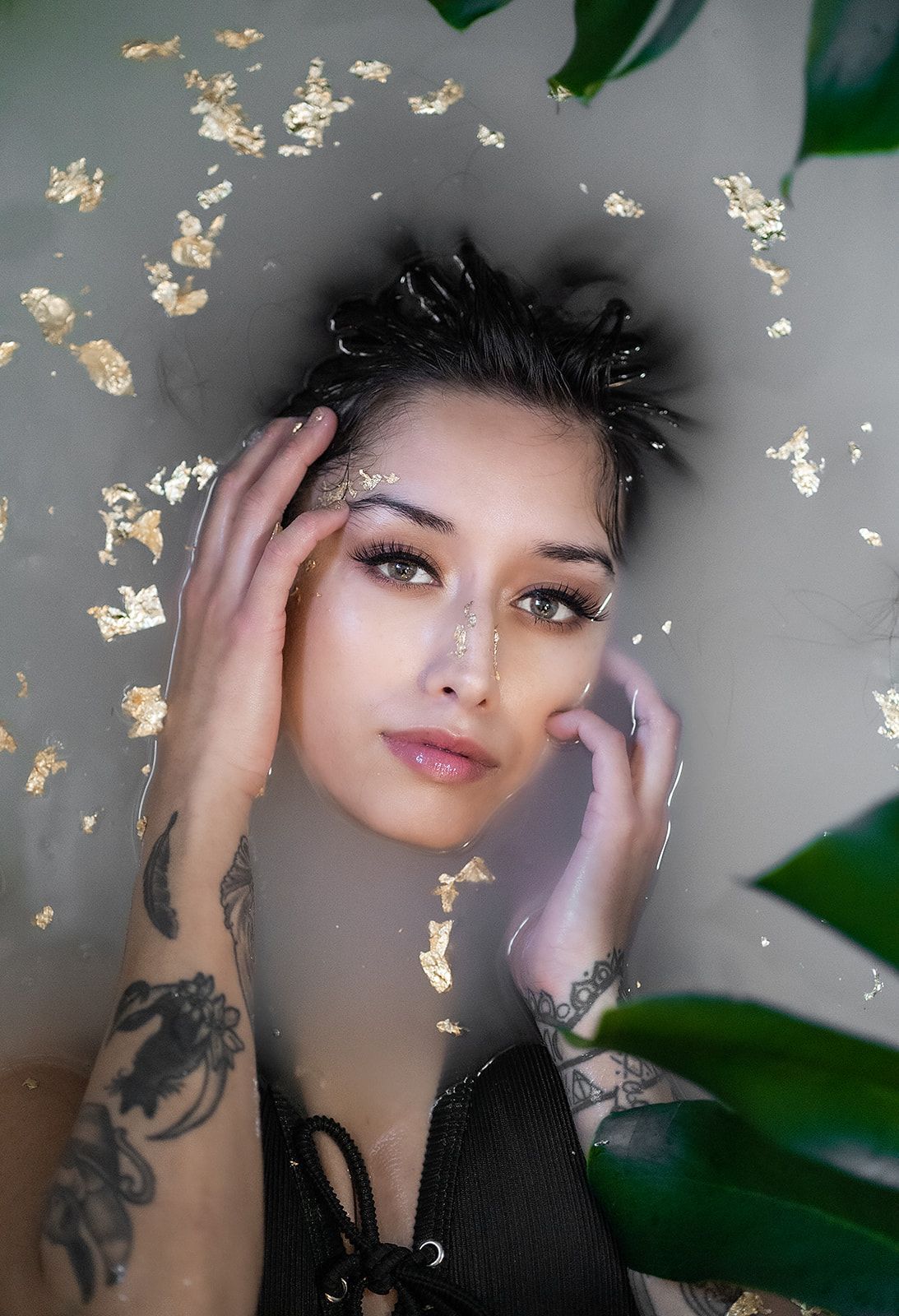 A woman is laying in a bathtub filled milk with water and gold leaves.