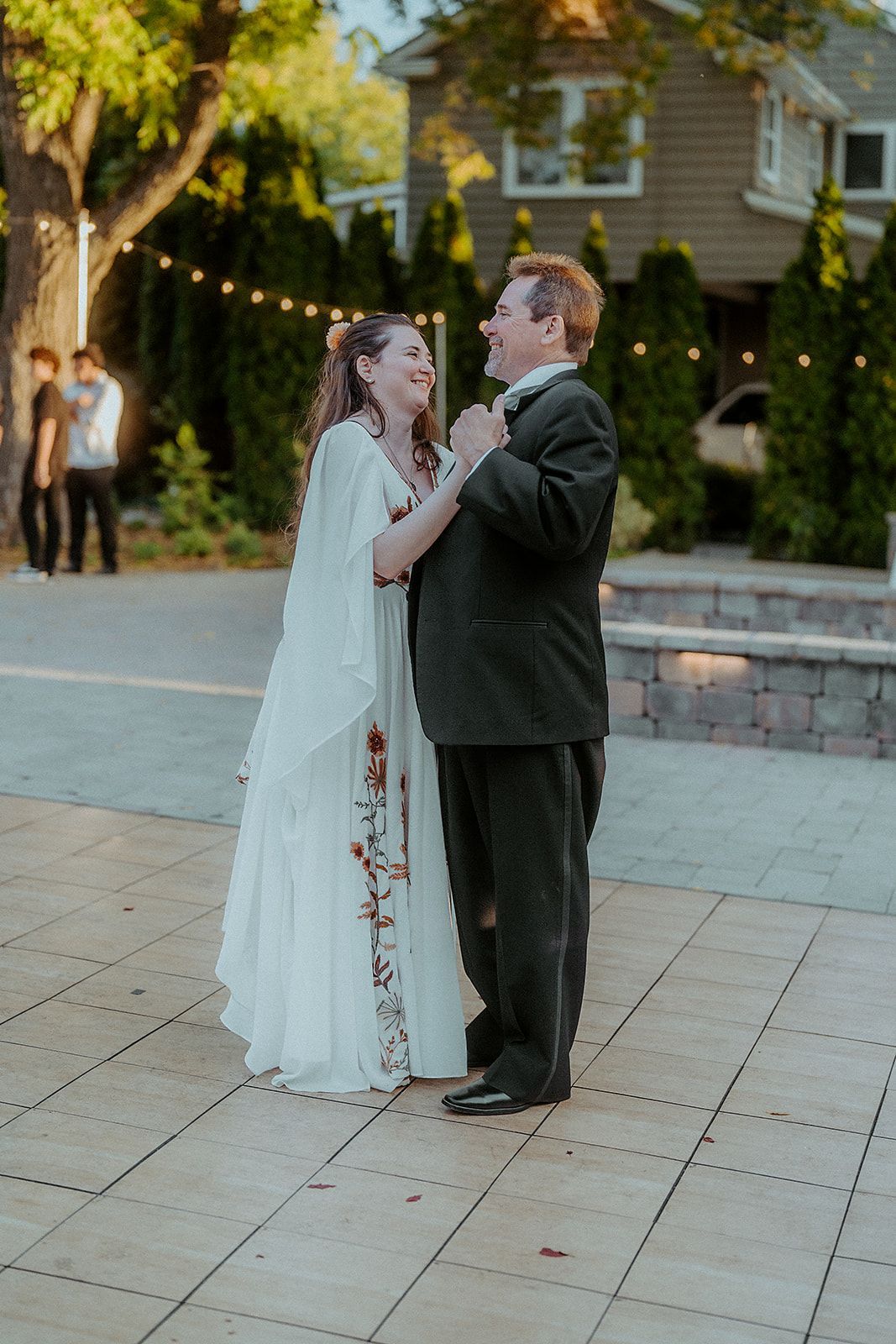 A bride and groom are dancing on a sidewalk in front of a house.