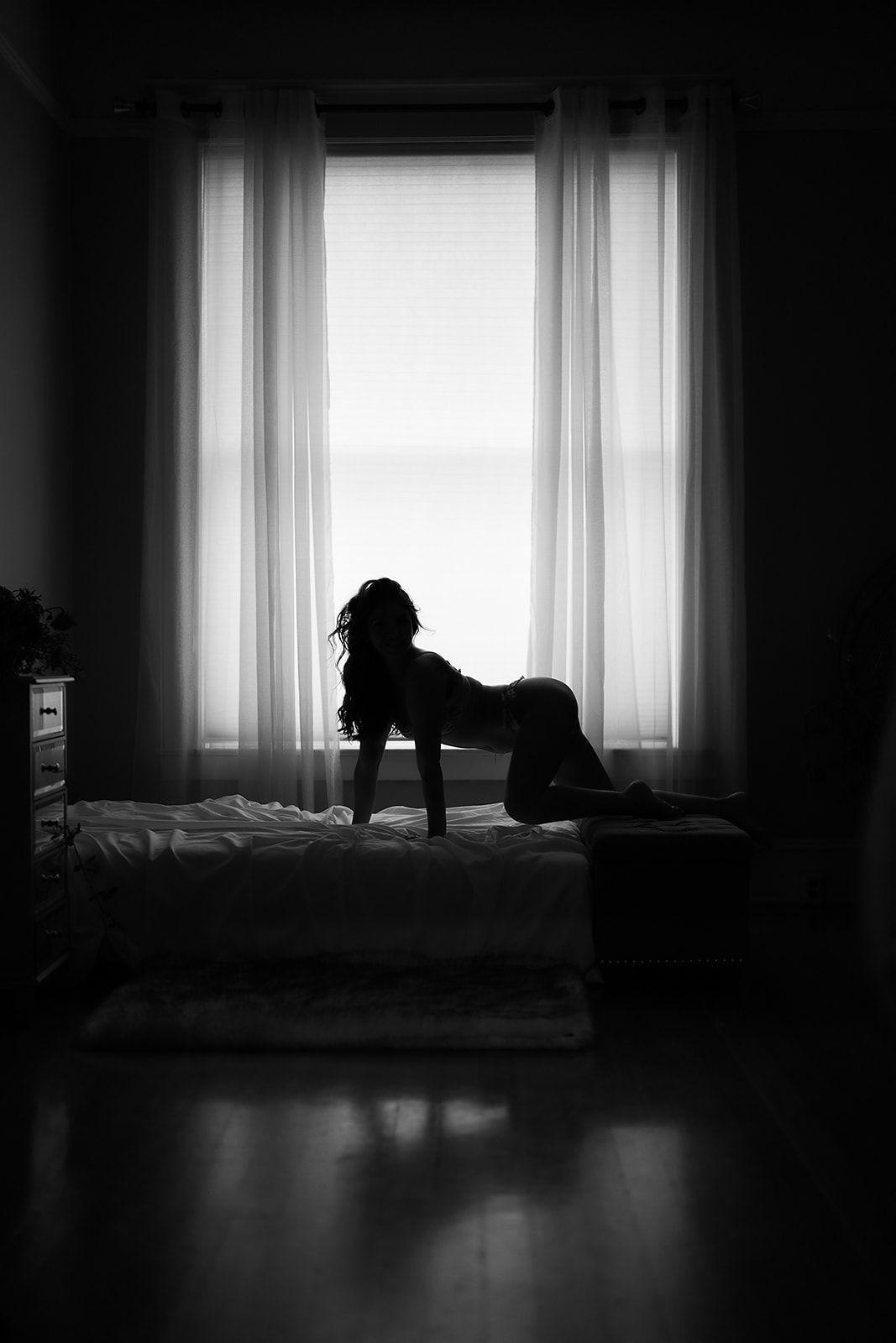 A woman is kneeling on a bed in front of a window in a black and white photo.