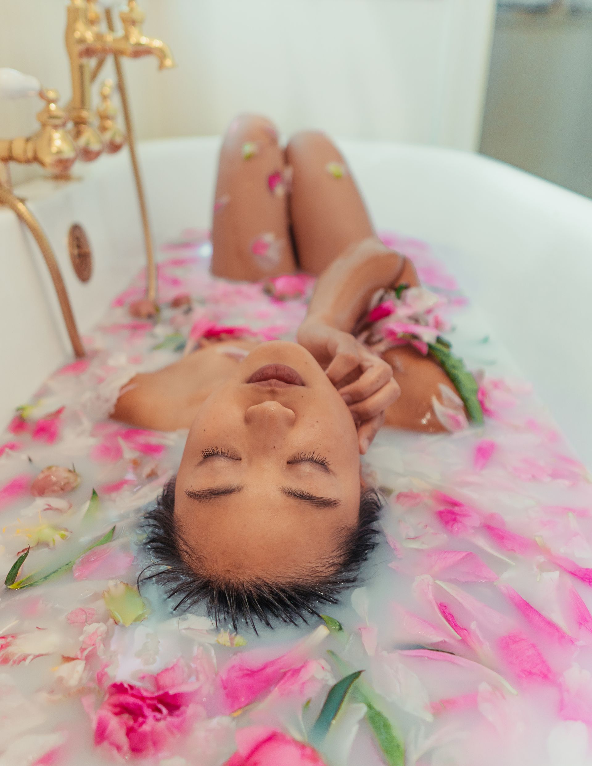 A woman is laying in a bathtub filled with pink flowers.