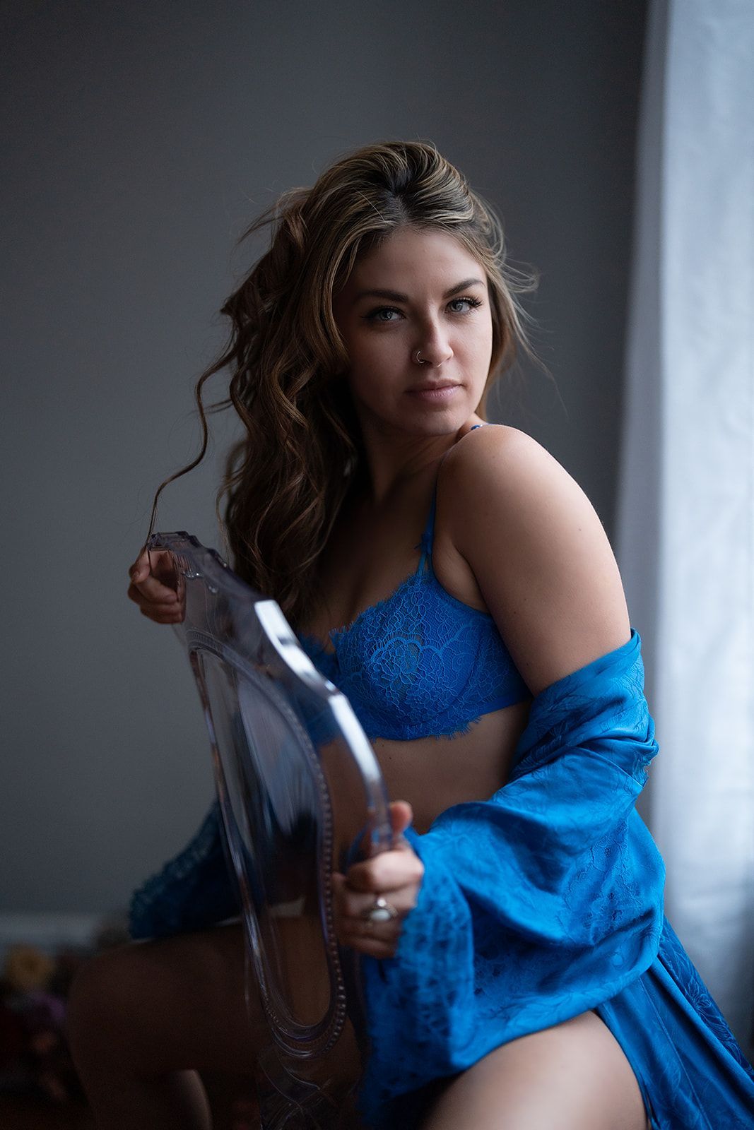 A woman in lingerie is sitting on a chair in front of a window.