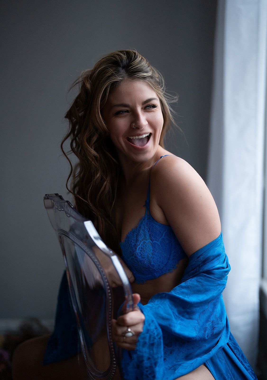 A woman in lingerie is sitting on a chair in front of a window.