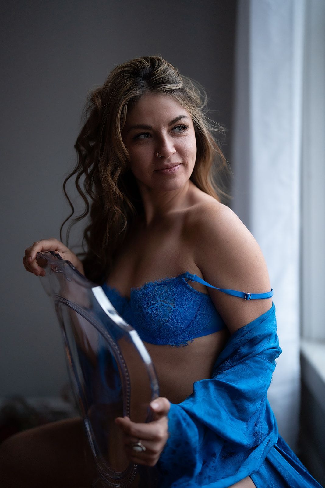 A woman in blue lingerie is sitting on a chair in front of a window.