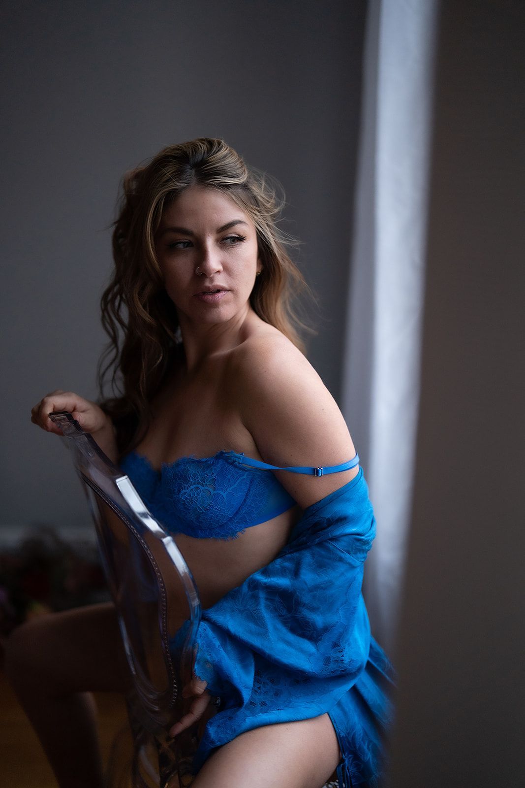 A woman in blue lingerie is sitting on a chair in front of a window.