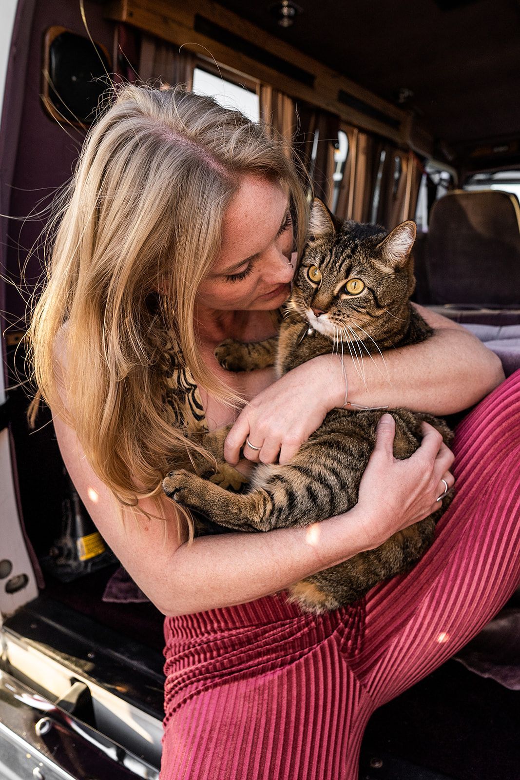 A woman is sitting in the back of a van holding a cat.