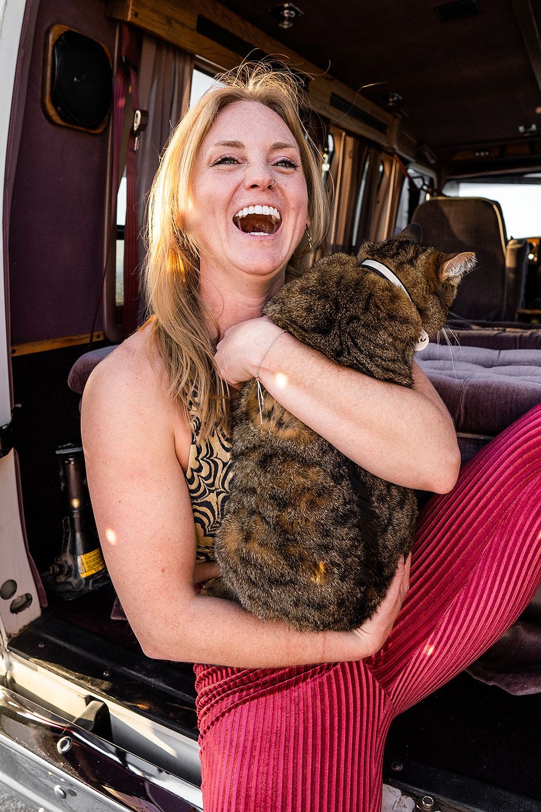 A woman is holding a cat in her arms in the back of a van.