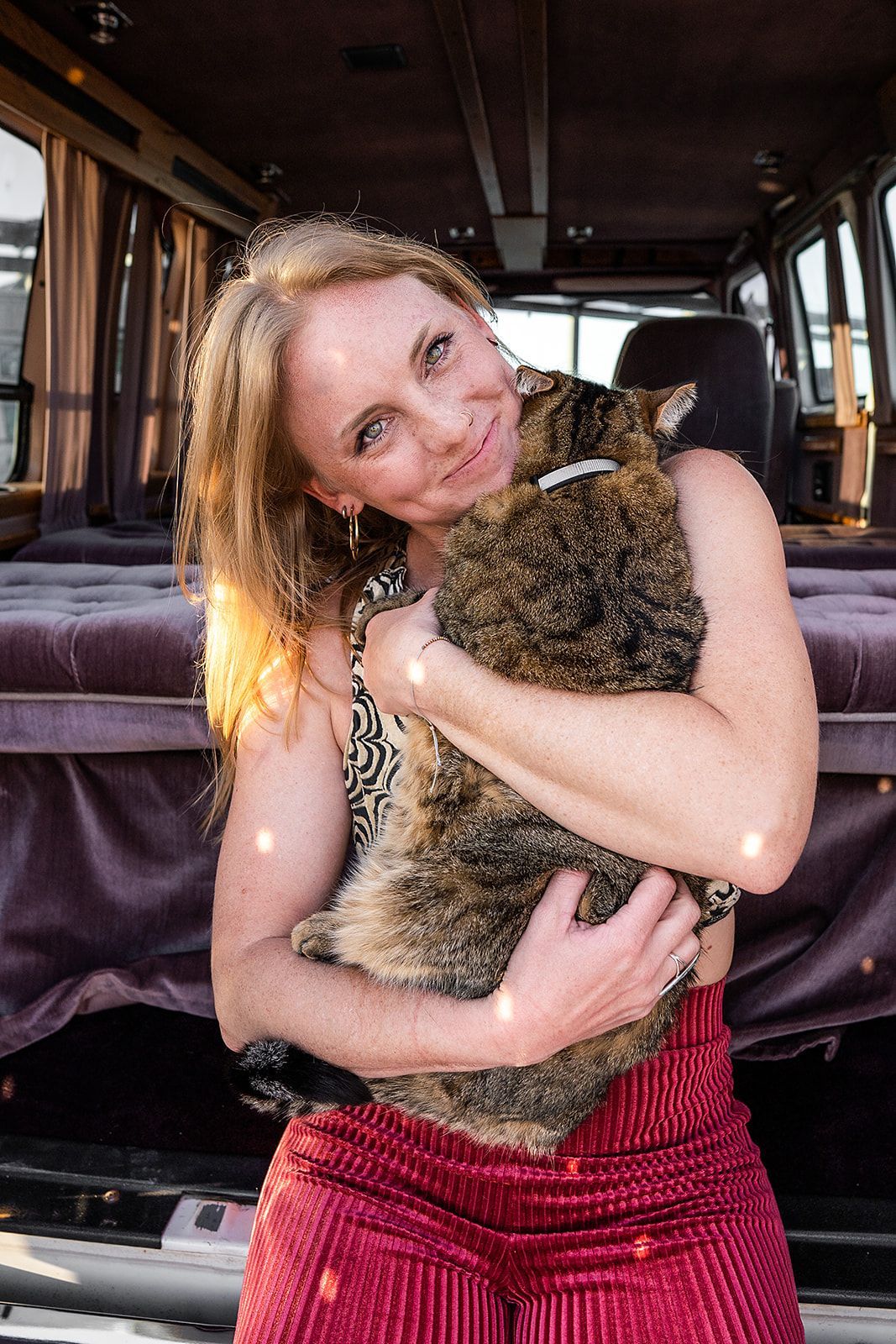 A woman is holding a cat in her arms in front of a bus.