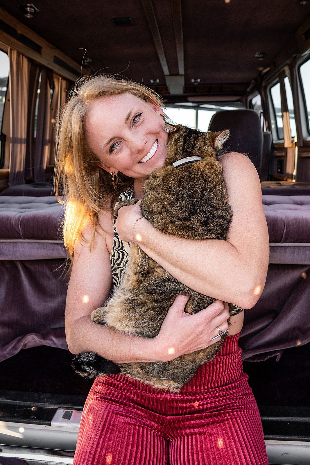 A woman is holding a dog in her arms in front of a van.