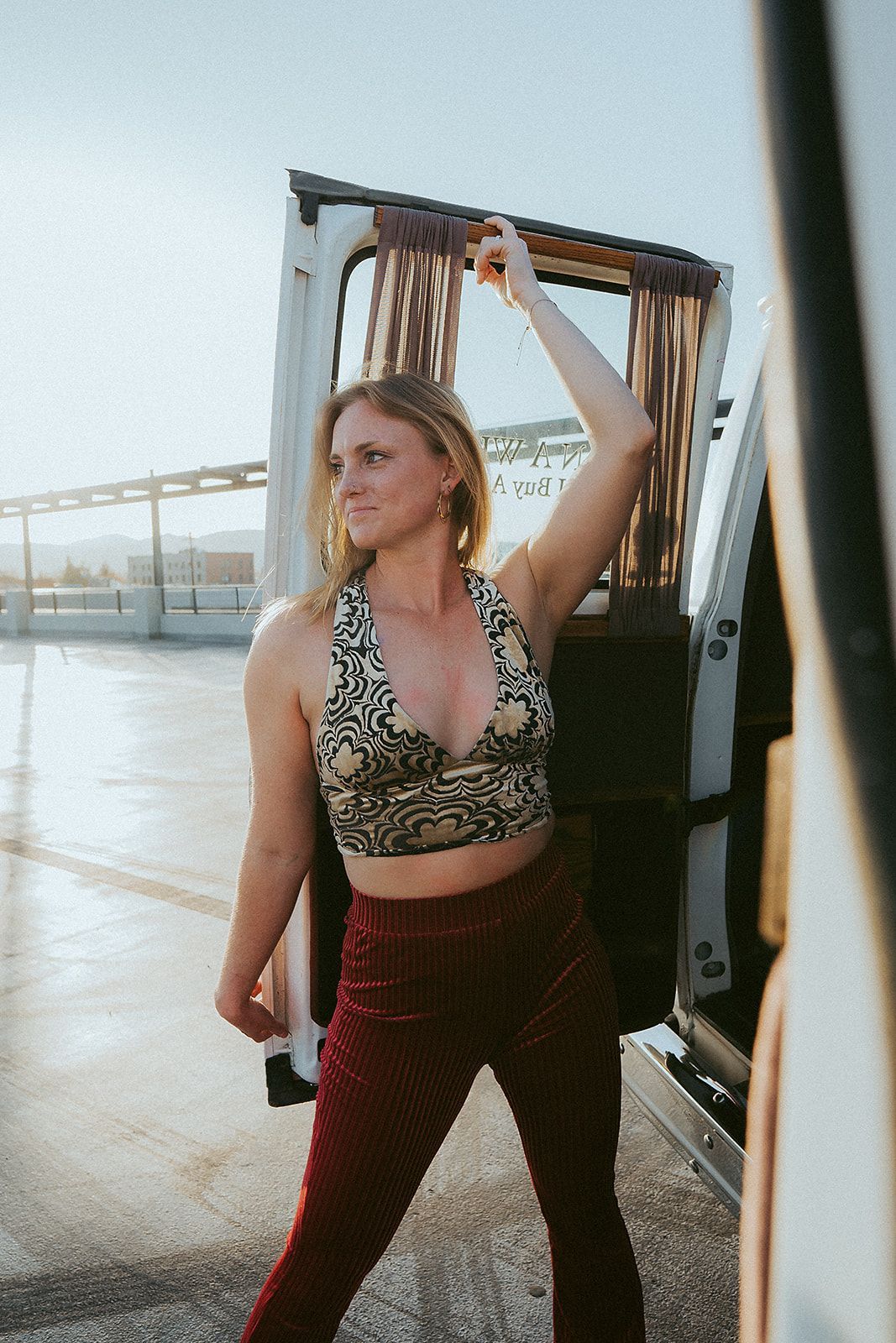 A woman in a crop top and red pants is standing next to a van.