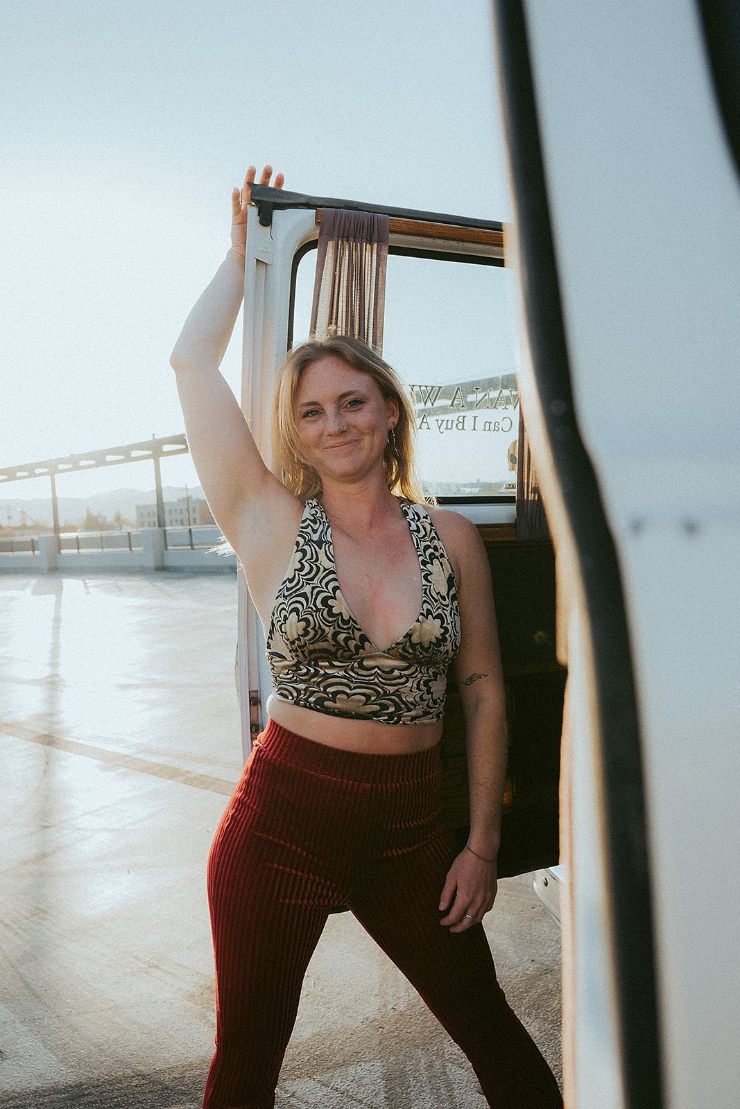 A woman in a crop top and red pants is standing next to a van.