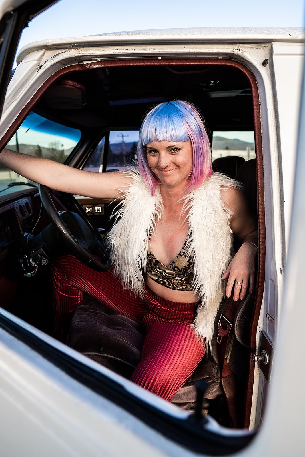 A woman with pink hair is sitting in the driver 's seat of a white truck.
