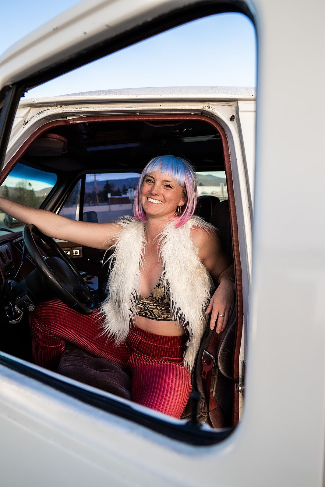 A woman in a pink wig is sitting in the driver 's seat of a white truck.
