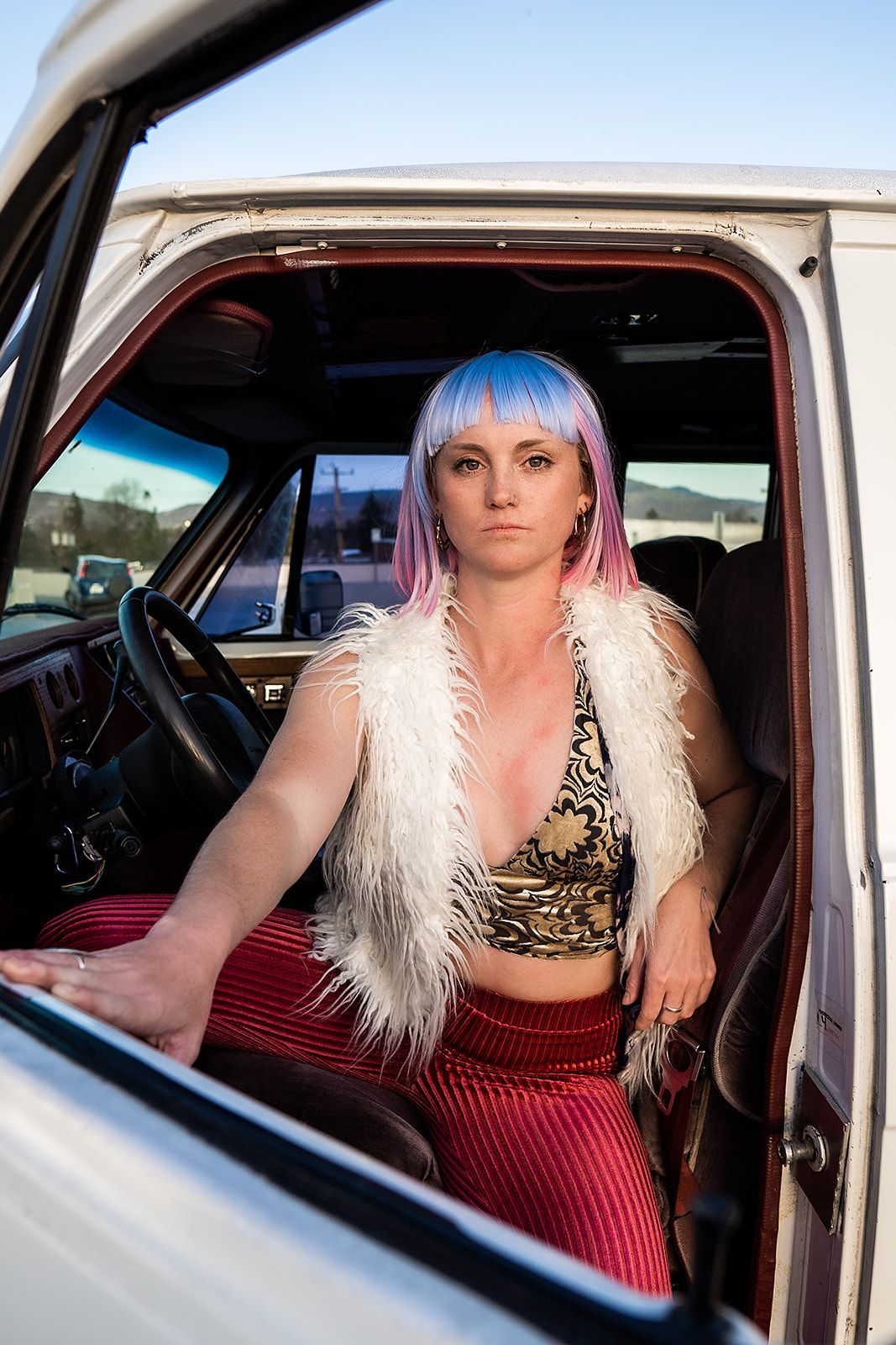 A woman with pink hair is sitting in the driver 's seat of a white truck.
