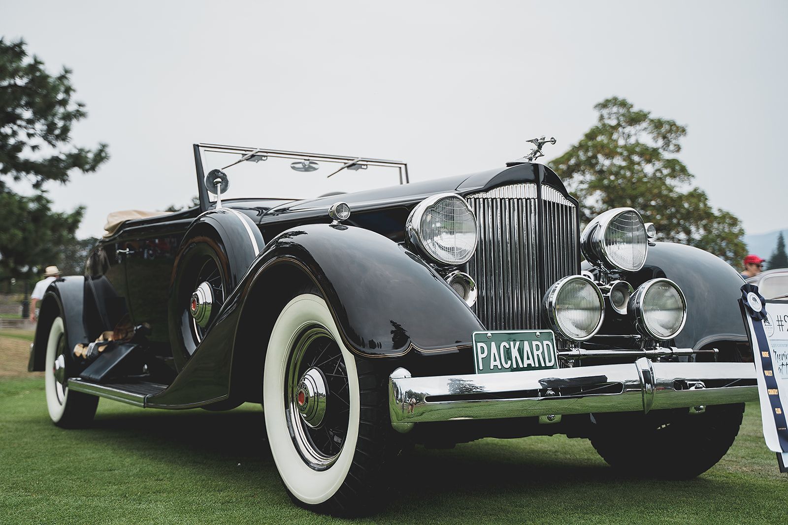 An old black car with white tires is parked on the grass.