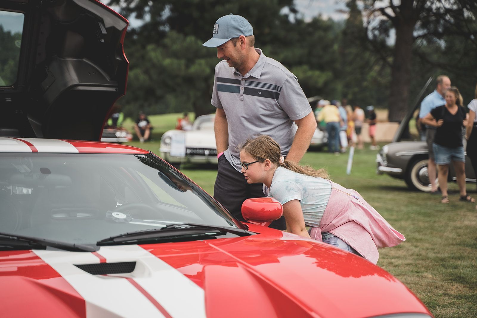 A man and a girl are looking at a red sports car at a car show.