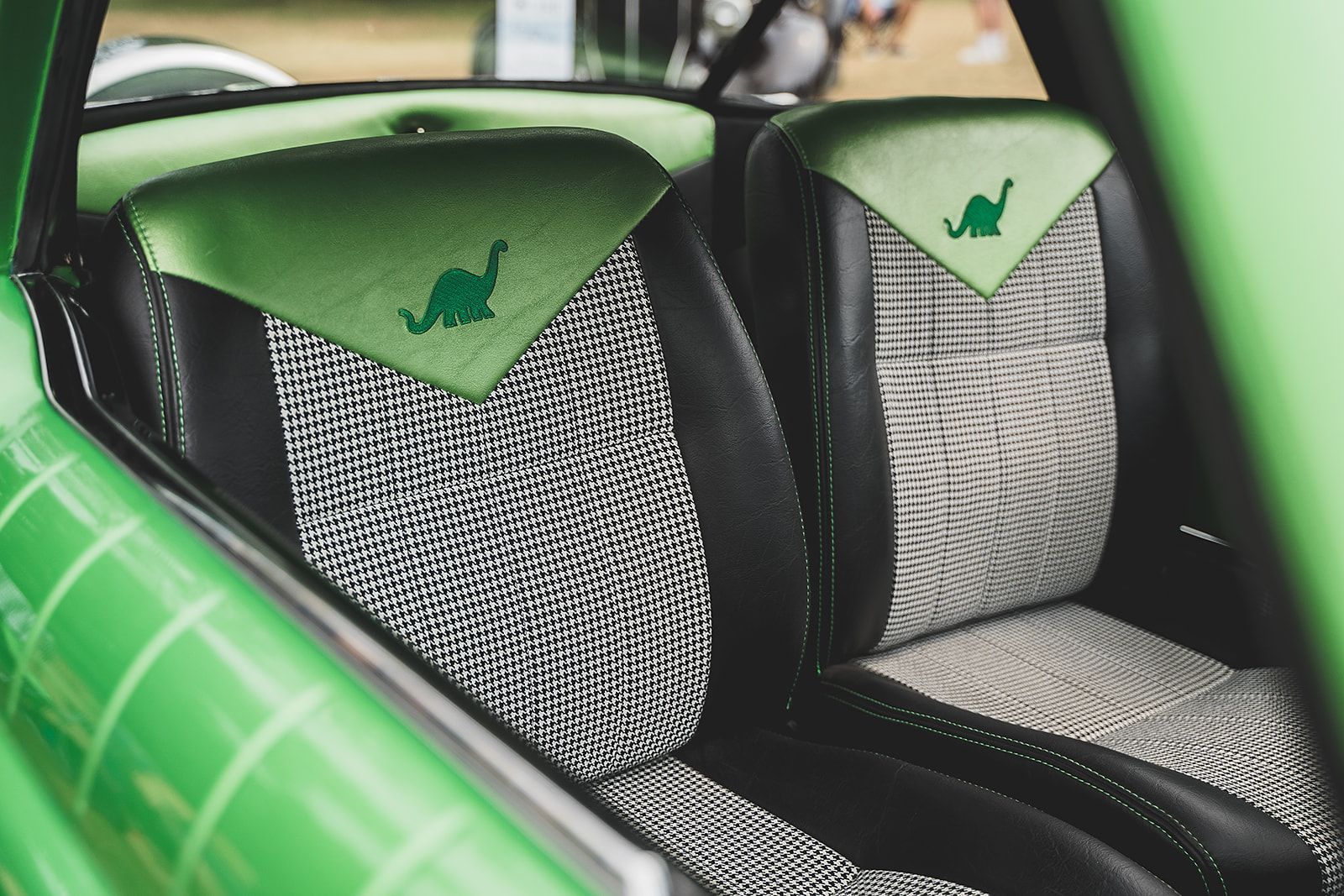 The back seat of a green car with a dinosaur embroidered on it.