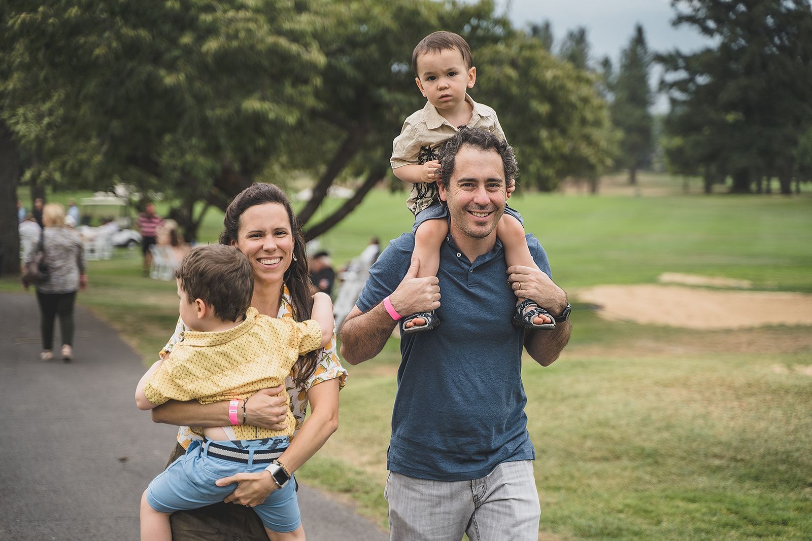 A man is carrying two children on his shoulders in a park.