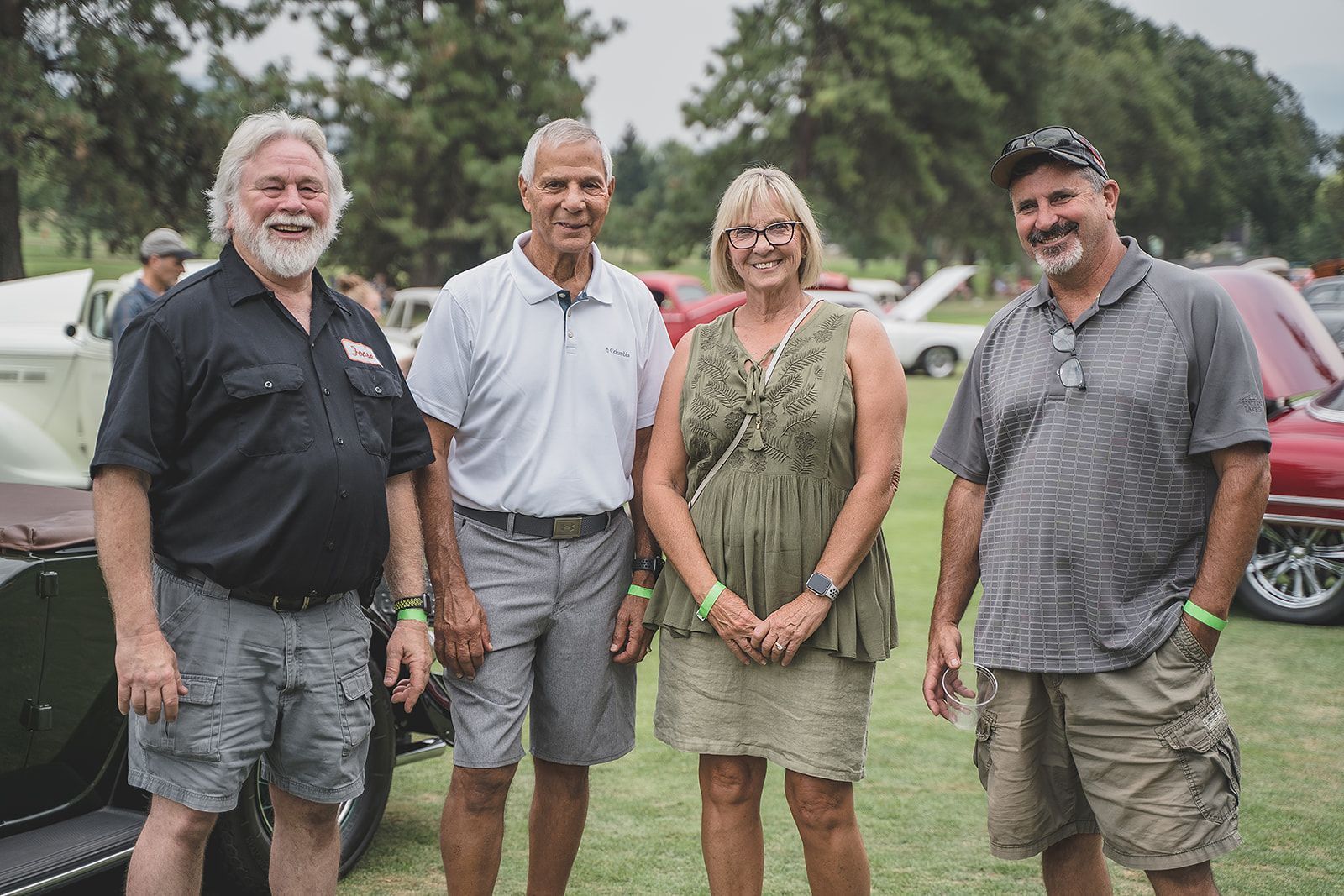 A group of people are posing for a picture in front of a car show.