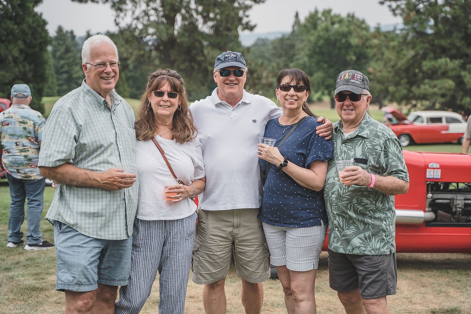 A group of people are posing for a picture in front of a red car.