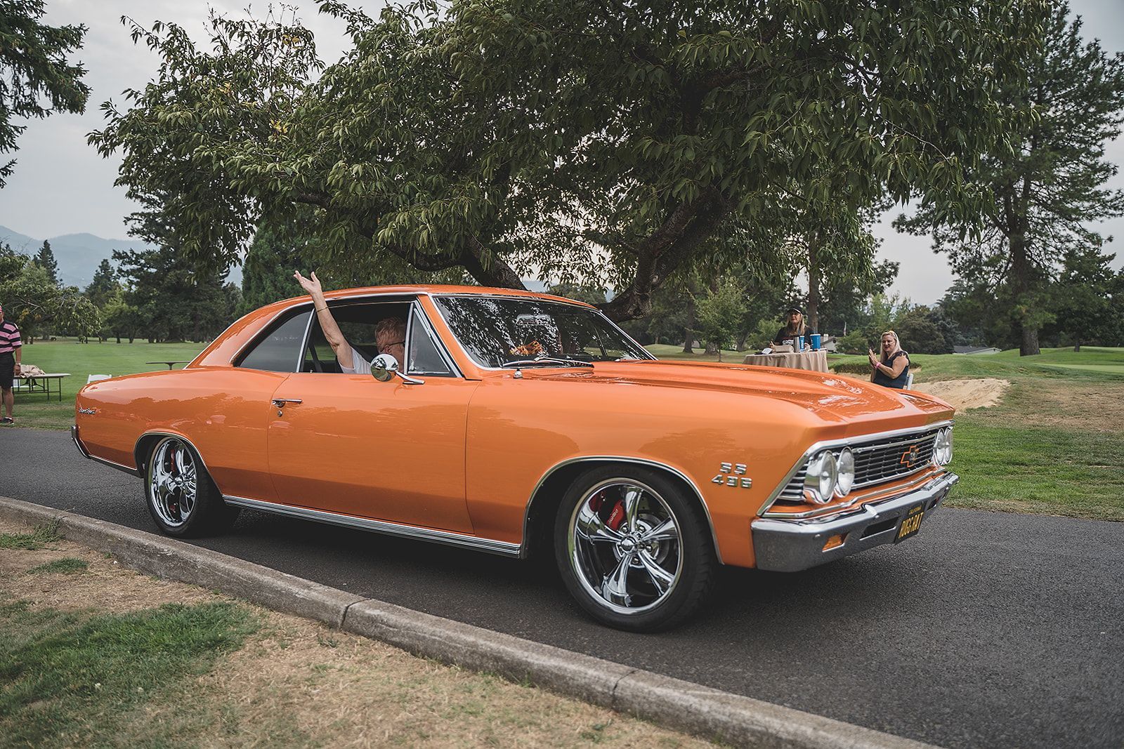 An orange car is parked on the side of the road in a park.