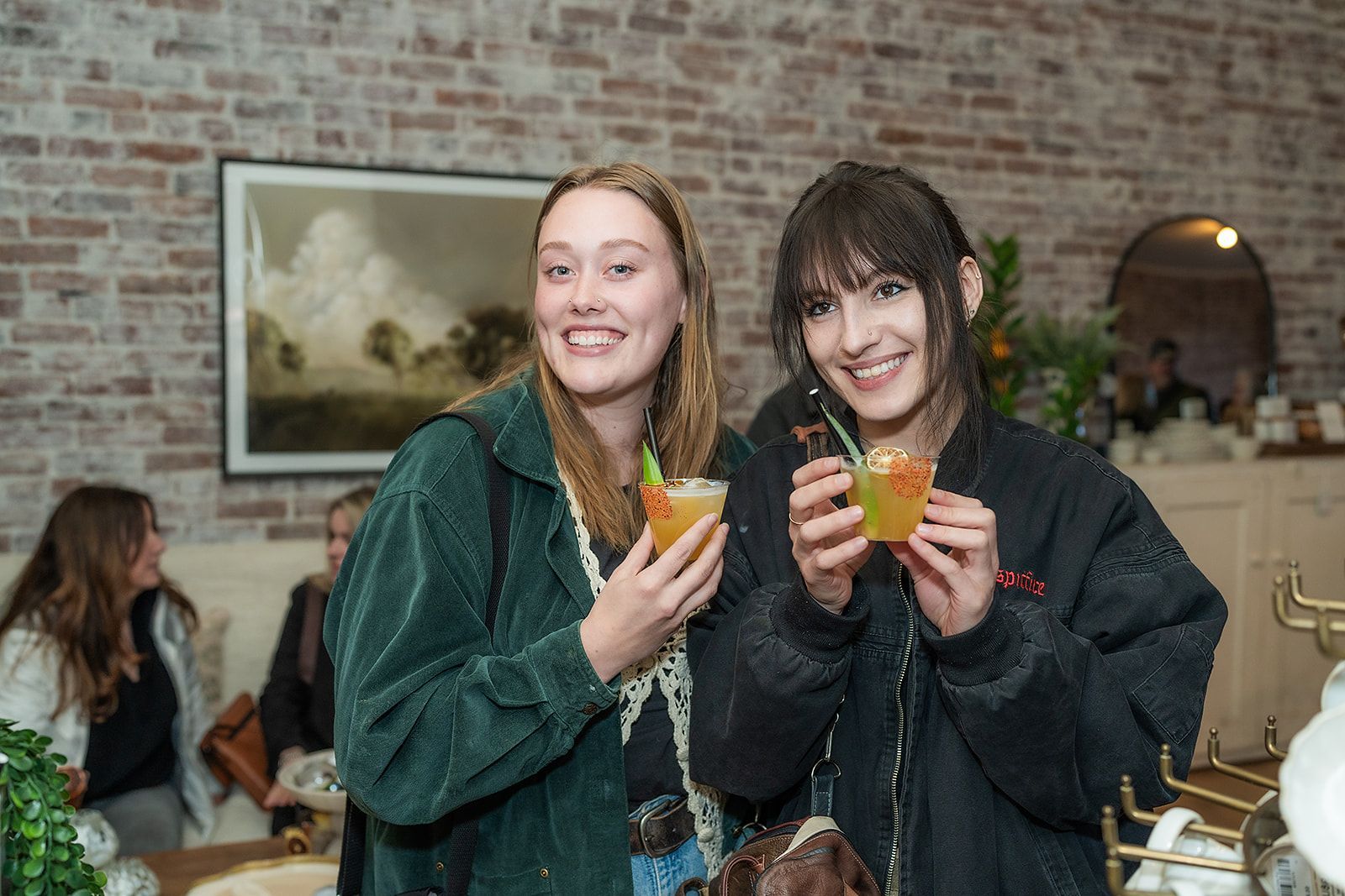 Two women are standing next to each other holding drinks in their hands.