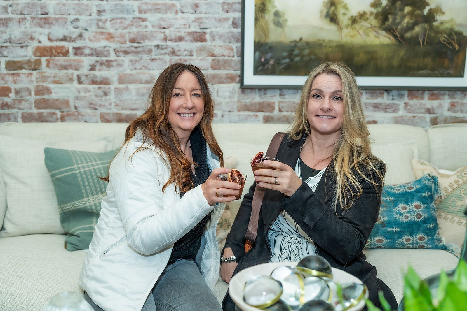 Two women are sitting on a couch holding cups of coffee.