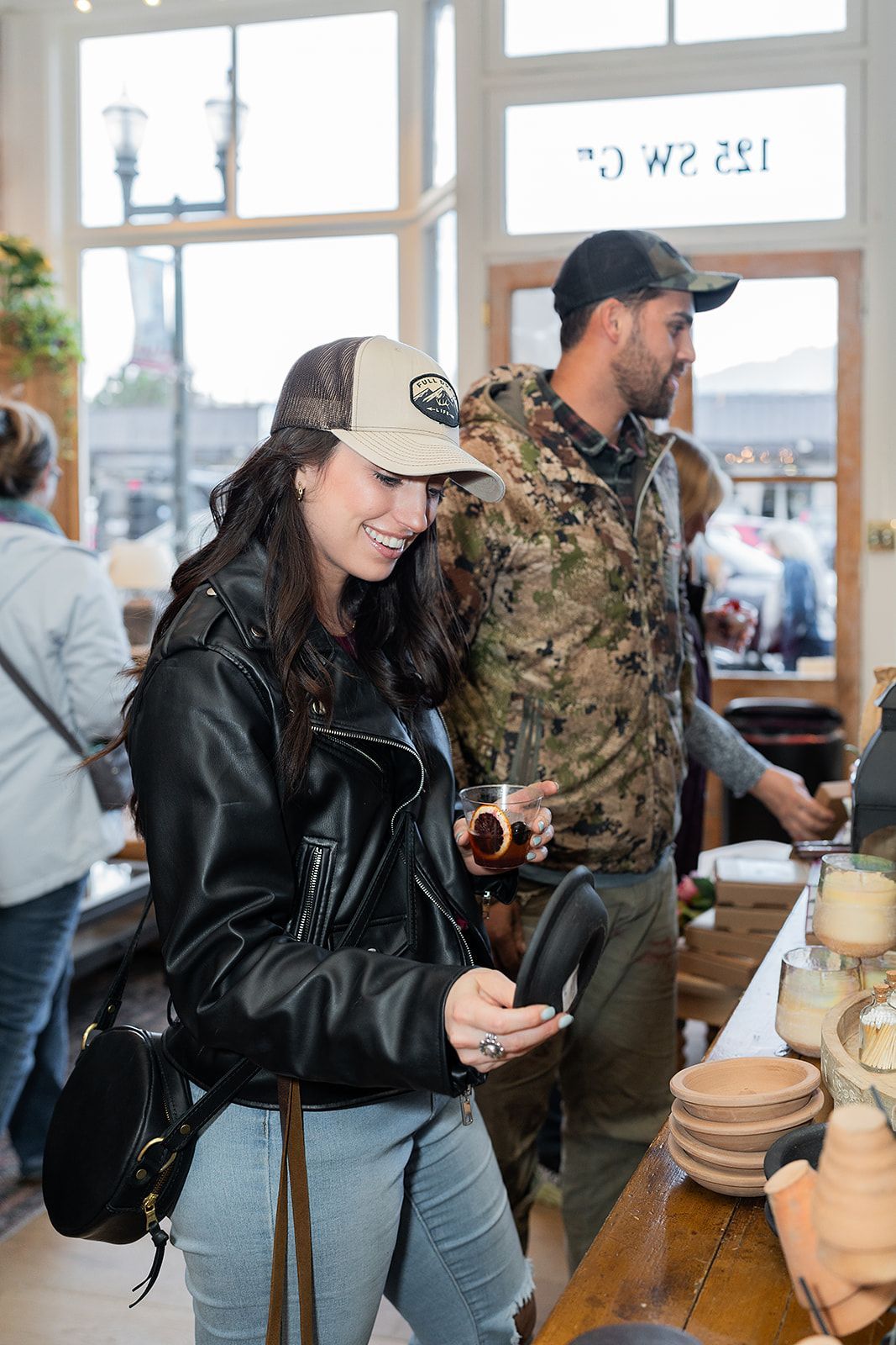 A man and a woman are standing in a restaurant looking at their phones.